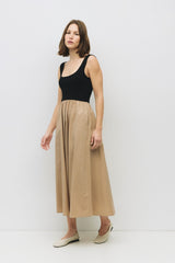 woman wearing a black sleeveless top and a beige midi skirt, standing against a white background
