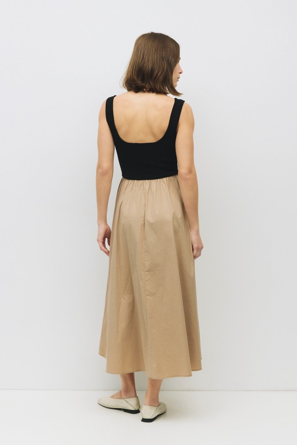 woman wearing a black tank top and a beige midi skirt, shown from the back