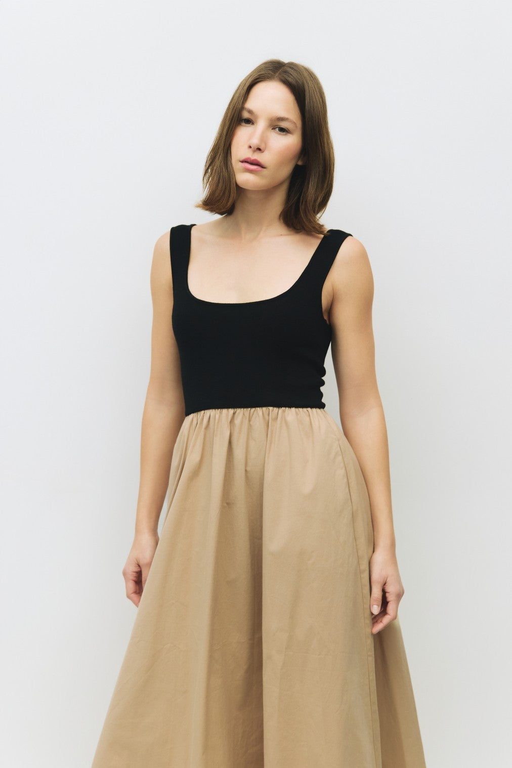 woman wearing a black sleeveless top with a scoop neckline and a beige flowy skirt