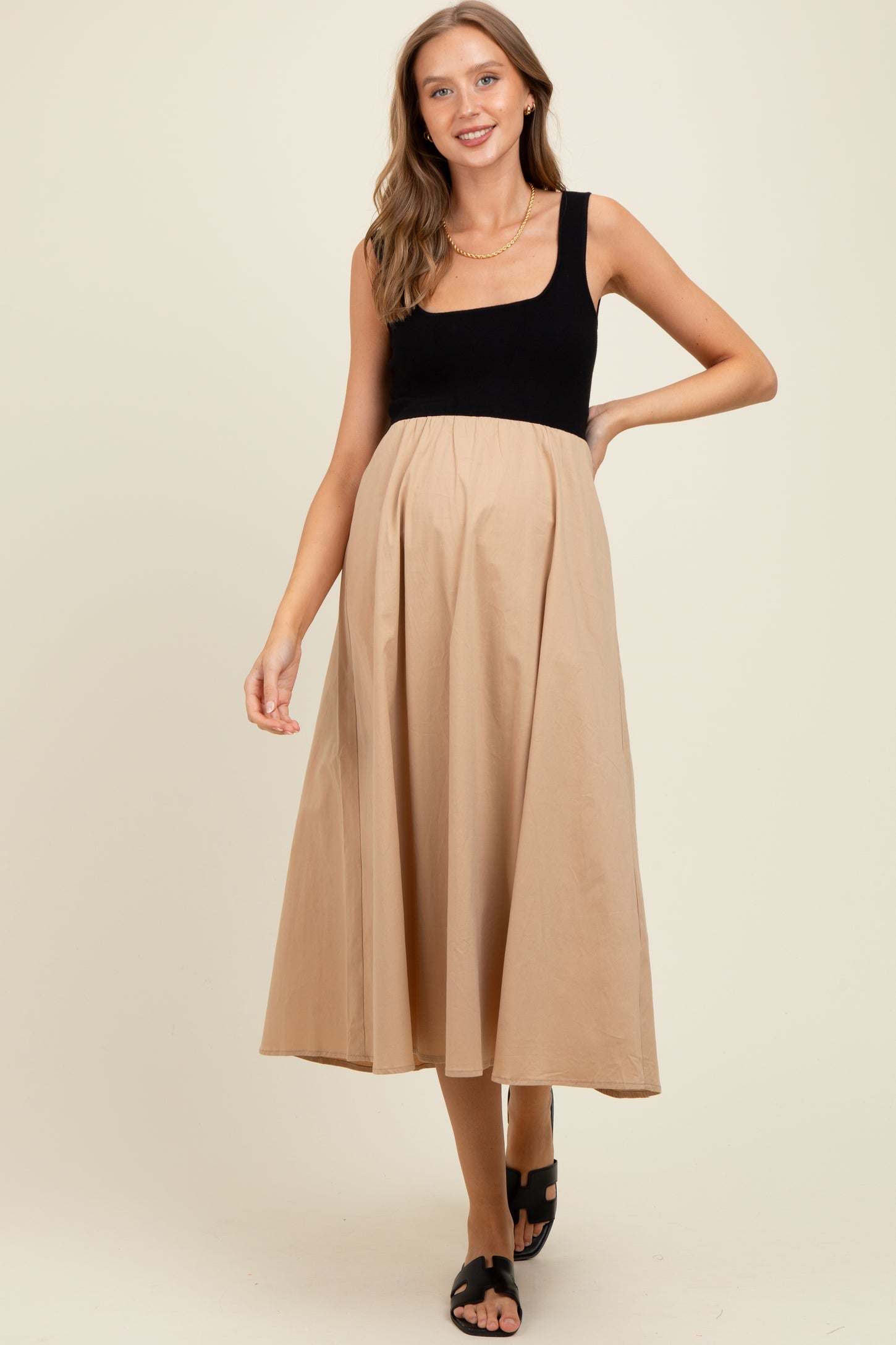 woman wearing a black and beige maternity dress with a square neckline and flowing skirt, showing her baby bump