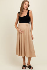 woman wearing a black sleeveless maternity dress with a beige skirt and holding her baby bump