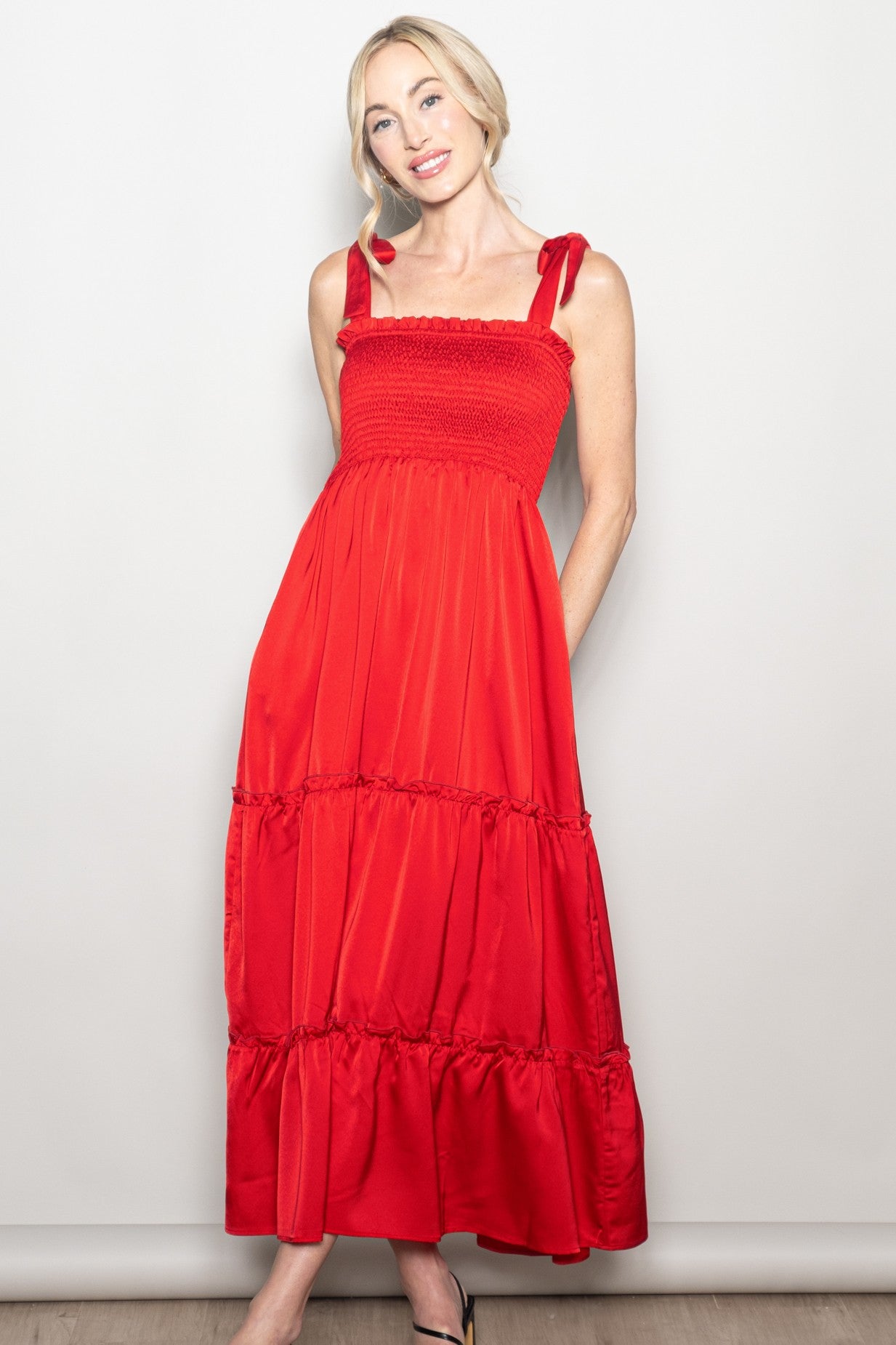 woman wearing a red maxi dress with smocked bodice and bow-tie straps, posing against a neutral background