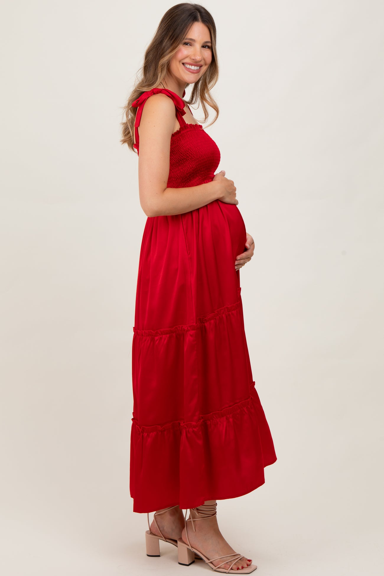 woman wearing a red maternity dress with ruffled straps and a tiered skirt, holding her baby bump