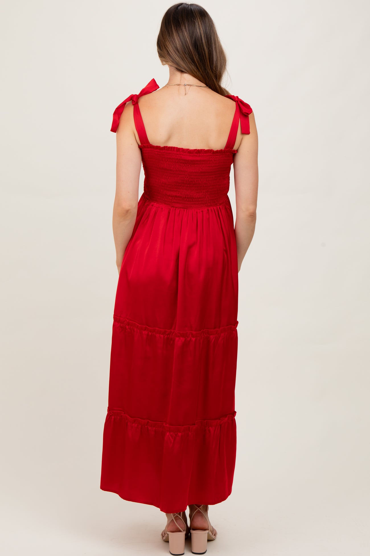 woman wearing a red maternity maxi dress with tie shoulder straps and a smocked bodice, viewed from the back