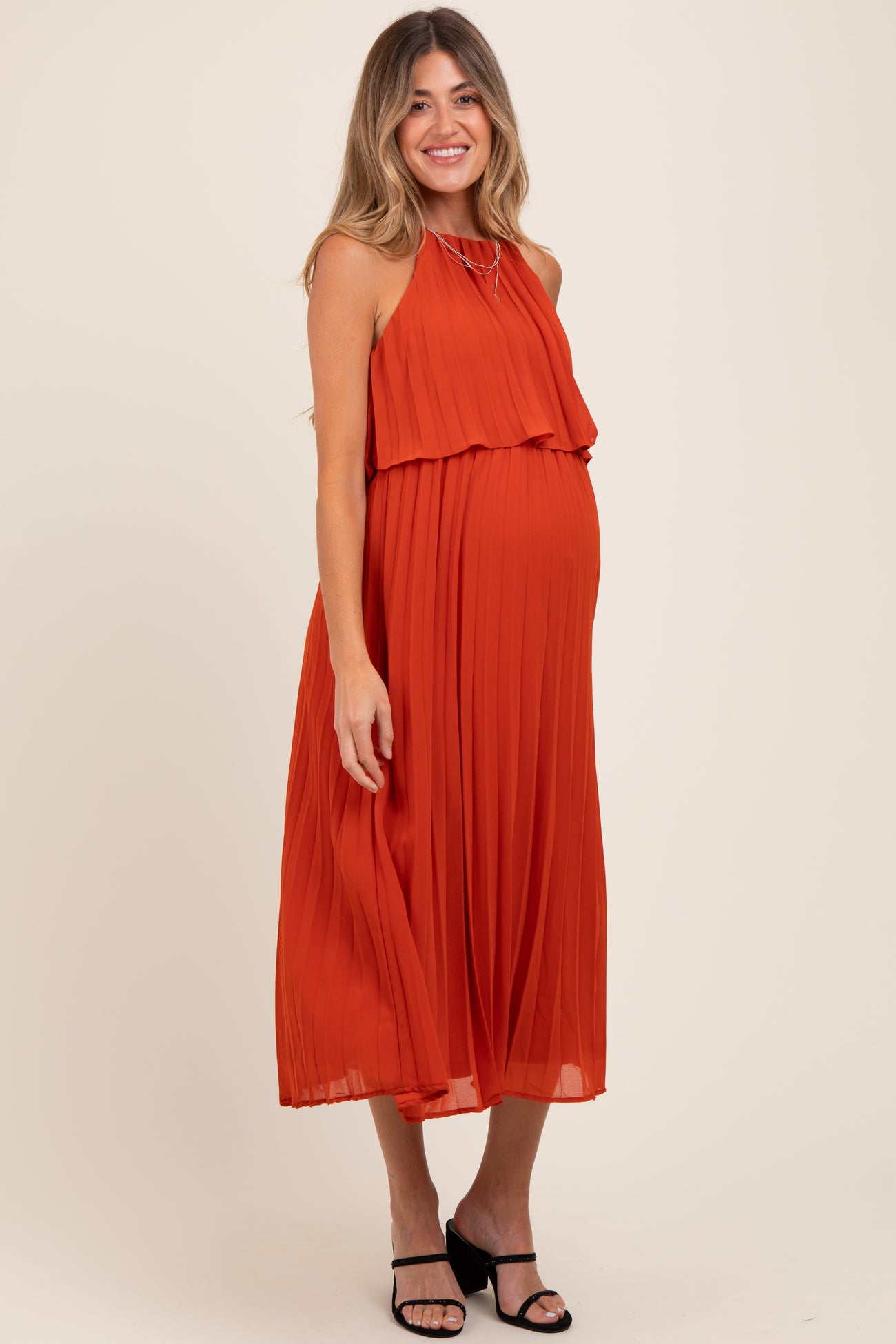 woman wearing a rust pleated maternity dress with a flowy silhouette and a visible baby bump