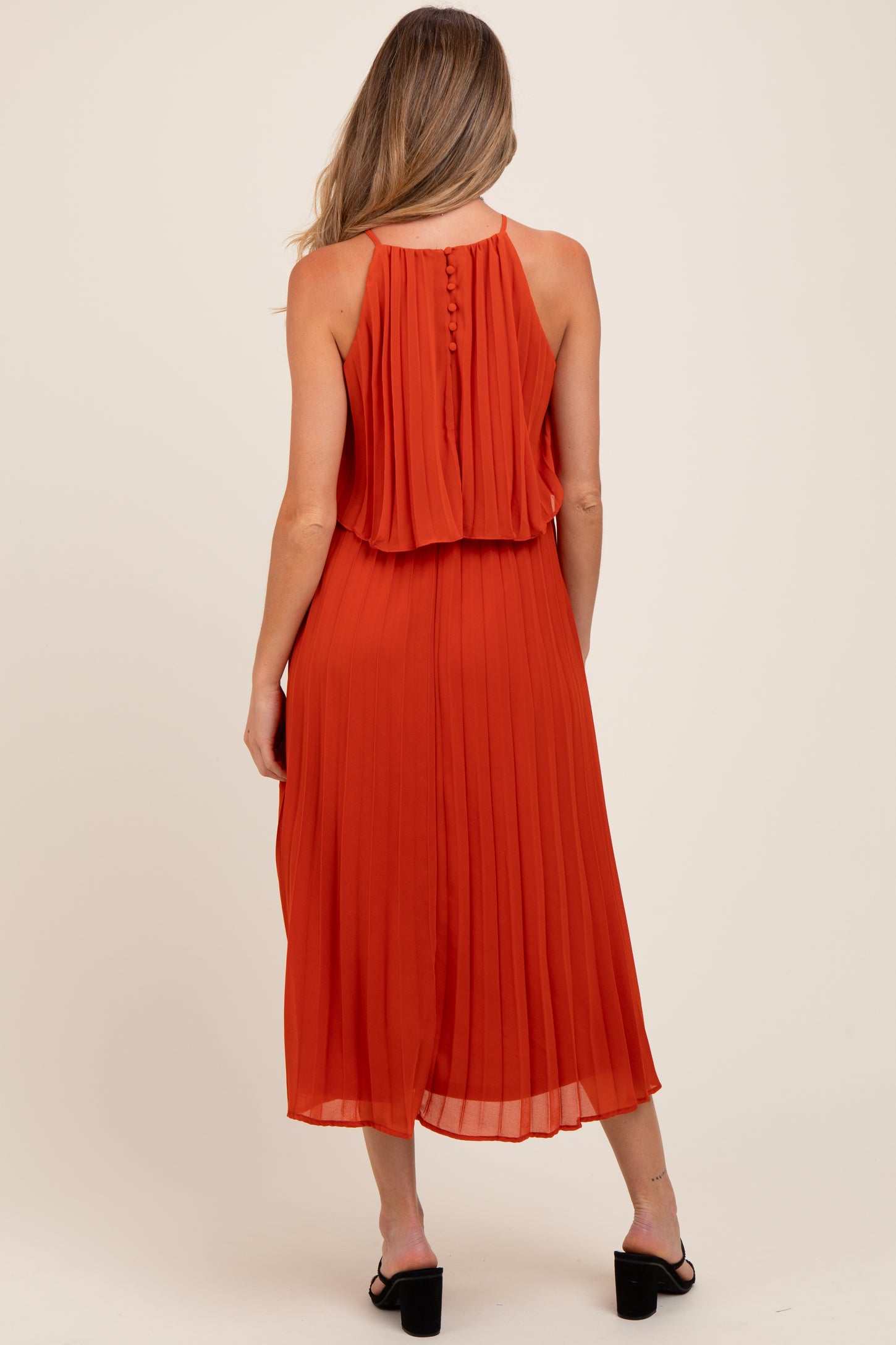 woman wearing a rust orange pleated maternity dress with a layered back and button details