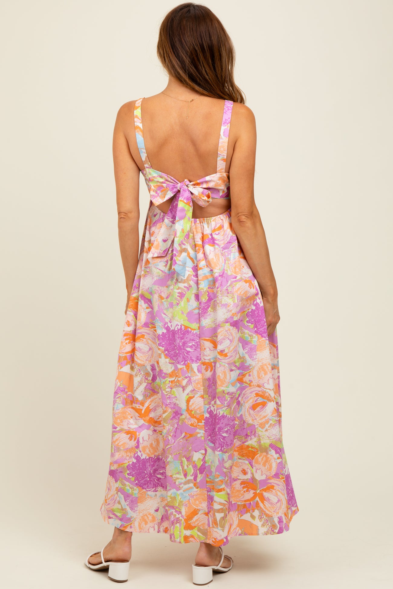 woman wearing a backless maxi dress with a floral print in pastel colors and a bow detail at the back