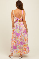 woman wearing a backless maxi dress with a floral print in pastel colors and a bow detail at the back