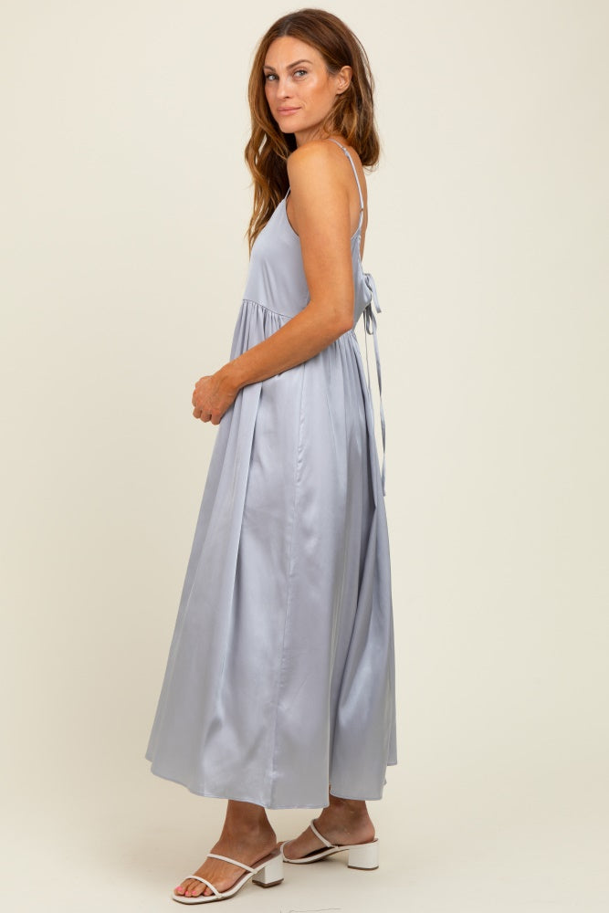woman wearing a light blue maxi dress with thin straps and a flowing skirt, standing sideways with a tie back detail