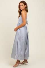 woman wearing a light blue maxi dress with thin straps and a flowing skirt, standing sideways with a tie back detail