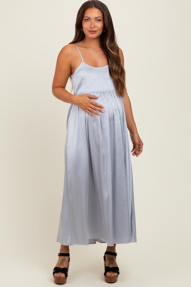 woman wearing a light gray satin maternity dress with a fitted bodice and flowing skirt, gently holding her baby bump
