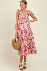 woman wearing a pink floral maternity maxi dress with tie straps and a smocked bodice, holding a straw handbag