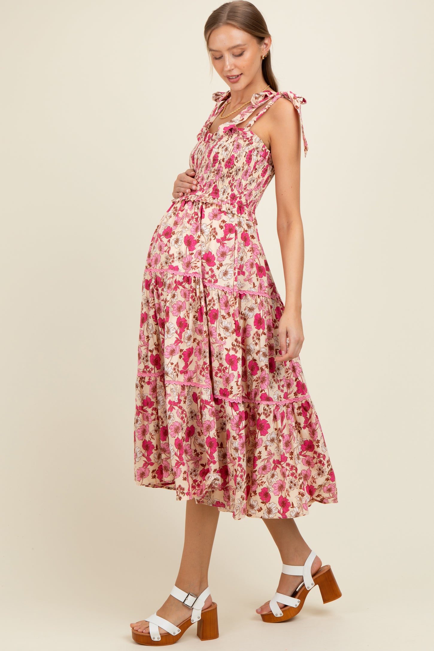 woman wearing a pink floral maternity dress with ruffled straps and a tiered skirt, highlighting her baby bump