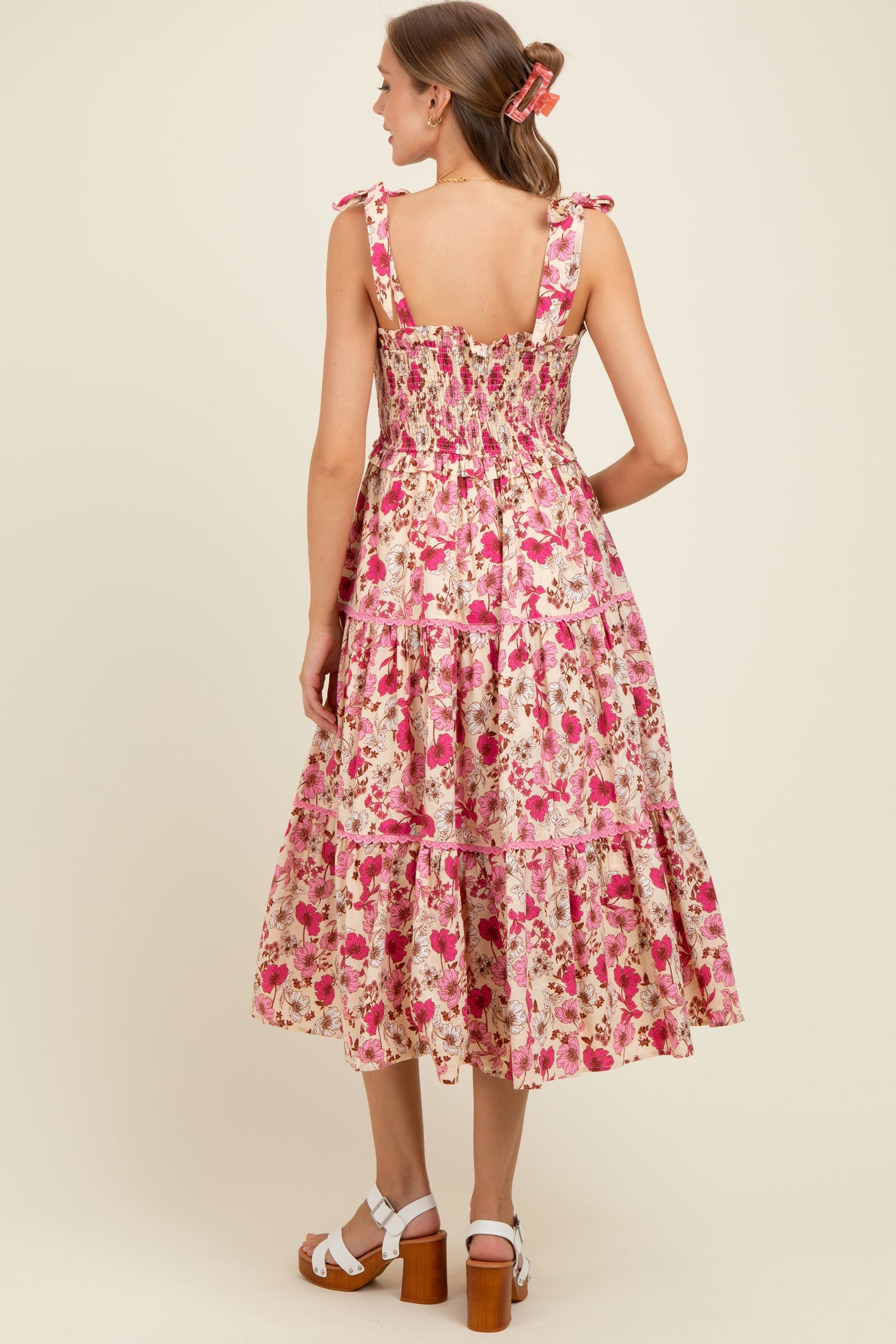 woman wearing a pink floral maternity dress with tie straps and a tiered skirt, showing a baby bump from the back