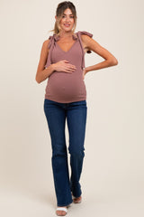 woman wearing a mauve maternity tank top with tie straps and blue flared jeans, holding her baby bump