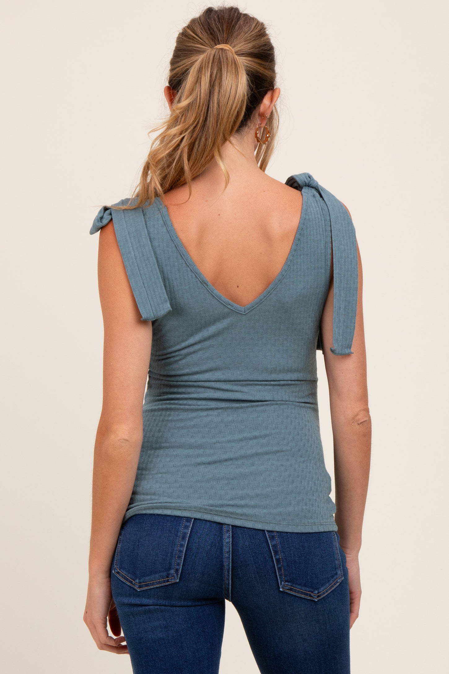 woman wearing a teal ribbed maternity top with tie shoulder straps and a v-back, paired with dark blue jeans