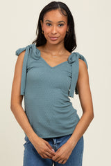 woman wearing a teal sleeveless top with tie details on the shoulders and a v-neckline