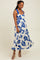 woman wearing a white maxi dress with a blue floral print and a fitted bodice, smiling and twirling