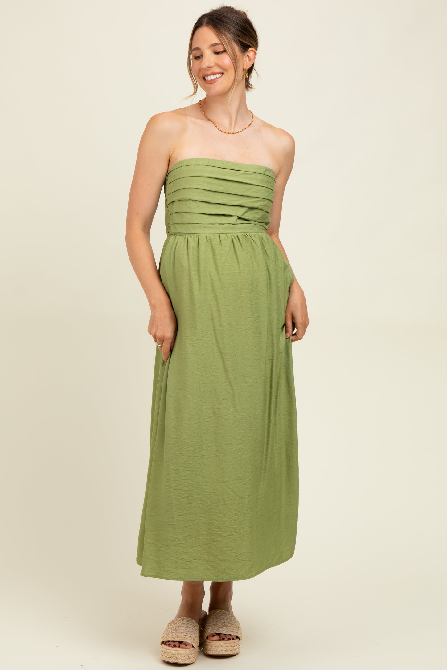 woman wearing a green strapless maternity maxi dress with gathered detail on the bodice and a relaxed fit