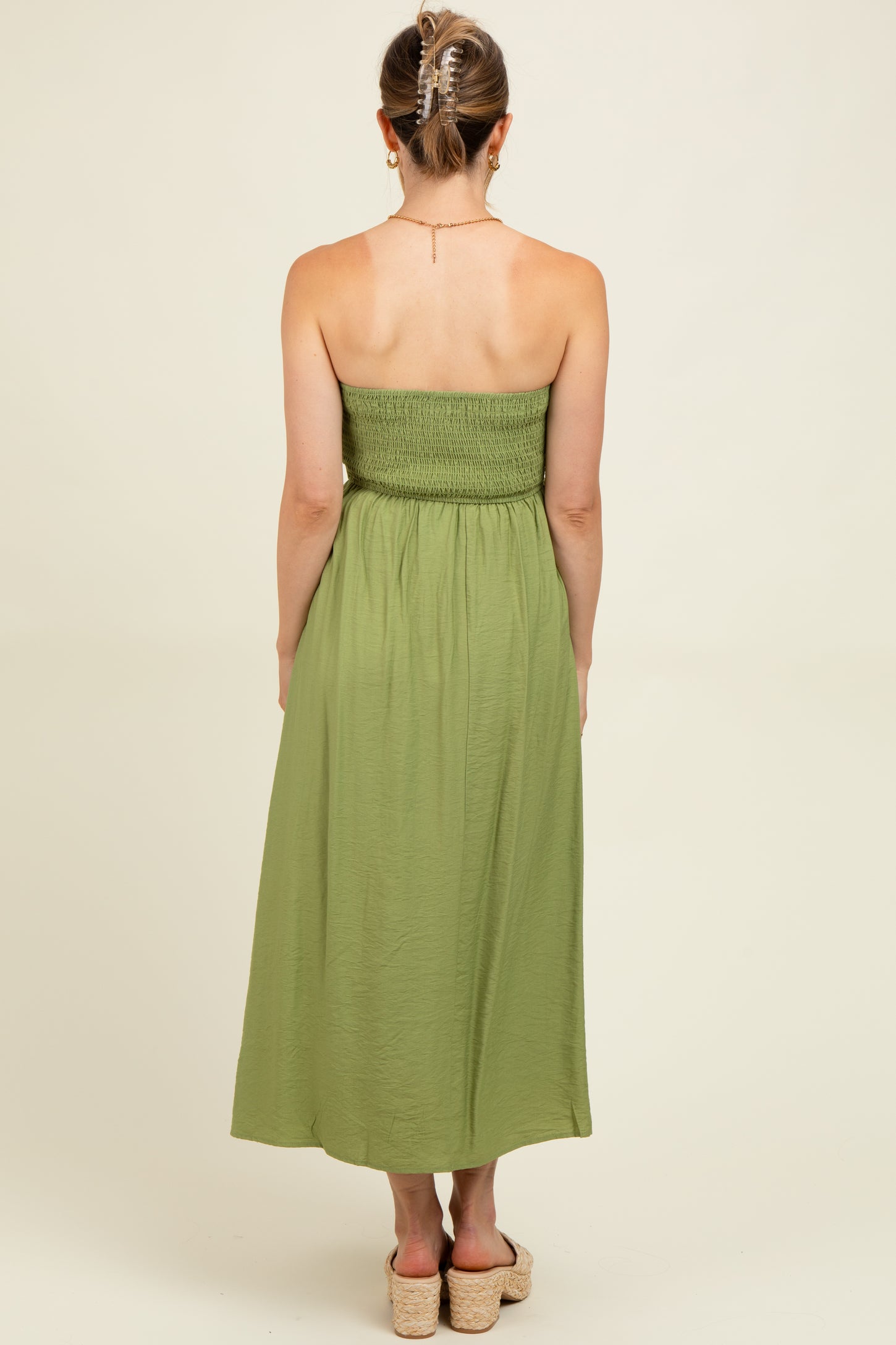 woman wearing a green maternity maxi dress with a smocked bodice and flowy skirt, viewed from the back