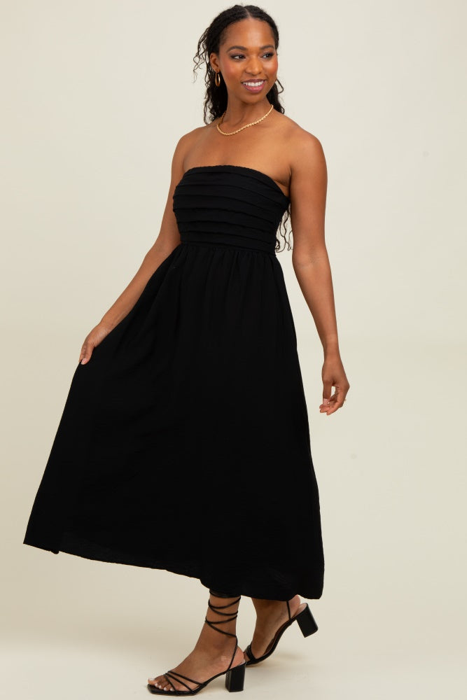 woman wearing a strapless black maxi dress with a gathered bodice and flowing skirt, styled with strappy sandals