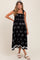 woman wearing a black maternity dress with floral print, smocked bodice, and tie straps, posing with a baby bump visible