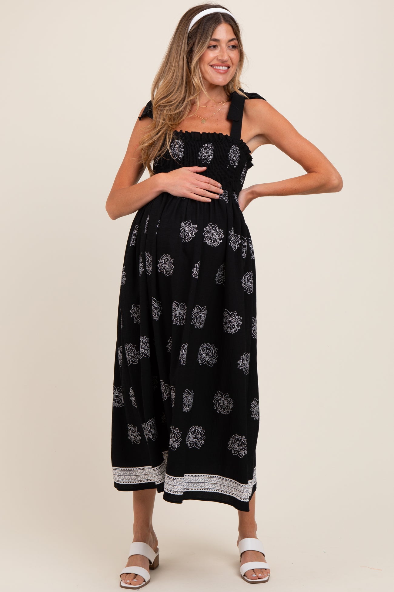 woman wearing a black floral maternity dress with smocked bodice and tie straps, showing her baby bump