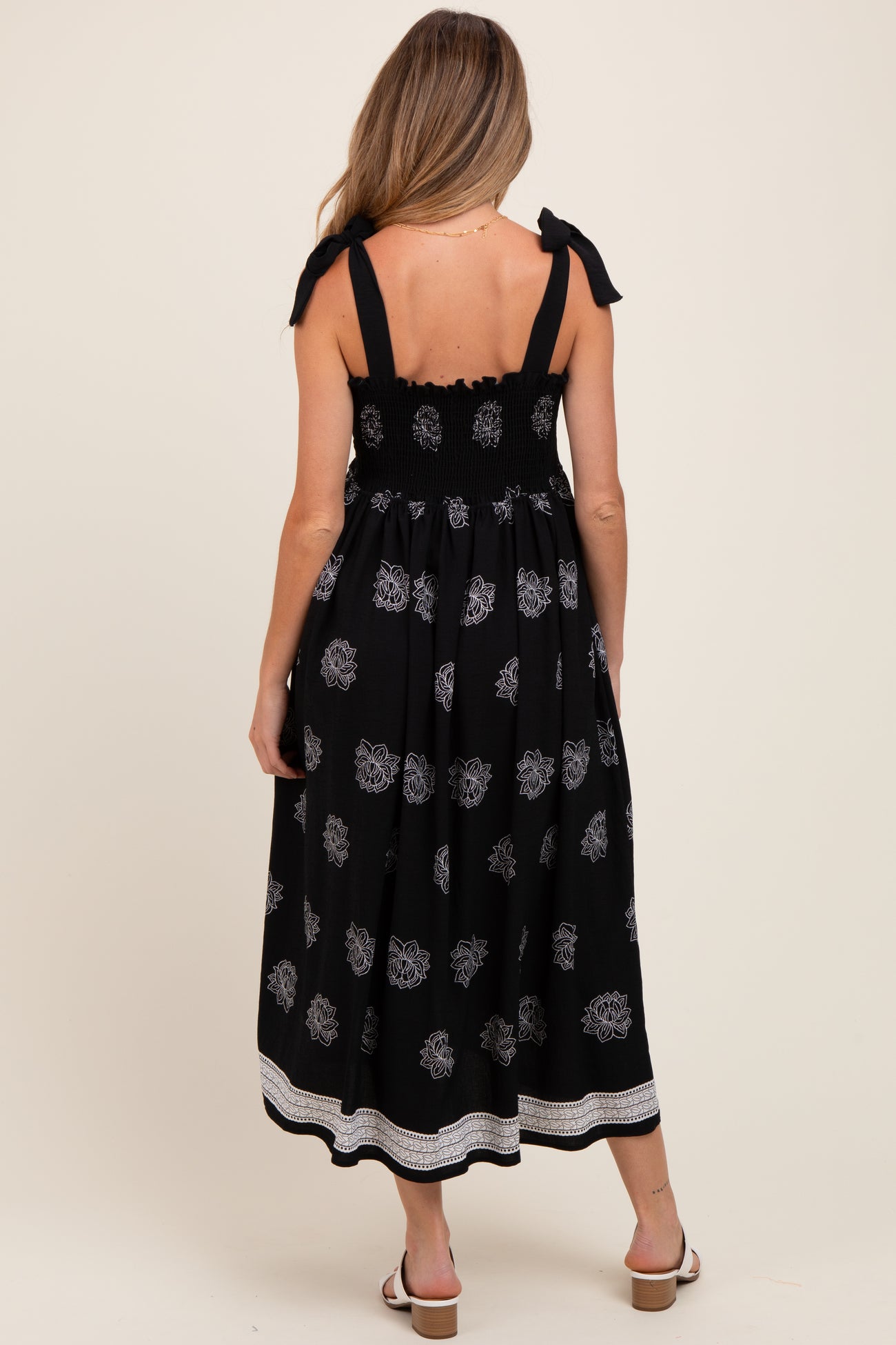 woman wearing a black maternity dress with floral print and tie straps, showing the back and smocked bodice detail