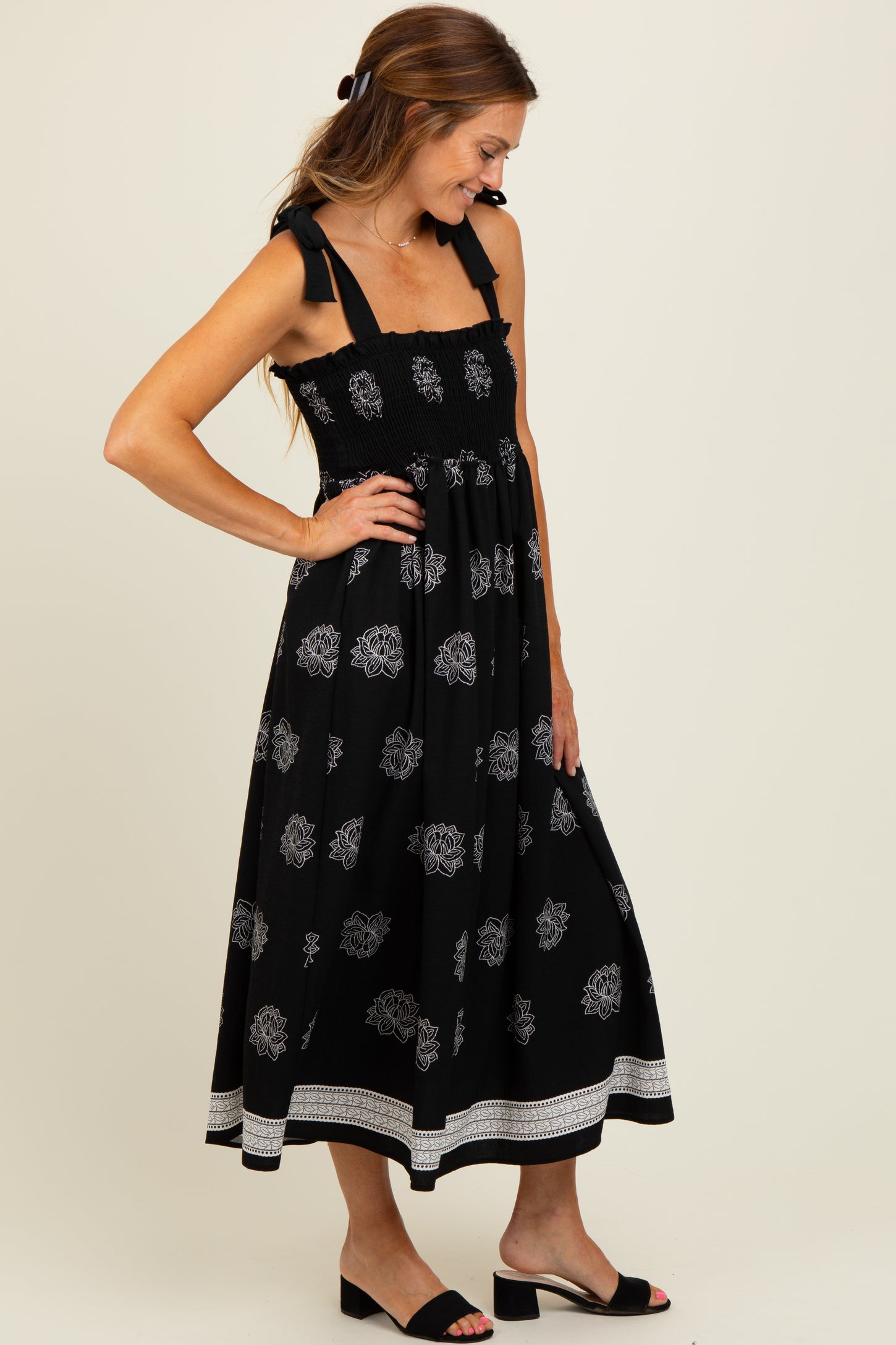 woman wearing a black floral print maxi dress with smocked bodice and bow straps, styled with black slide sandals