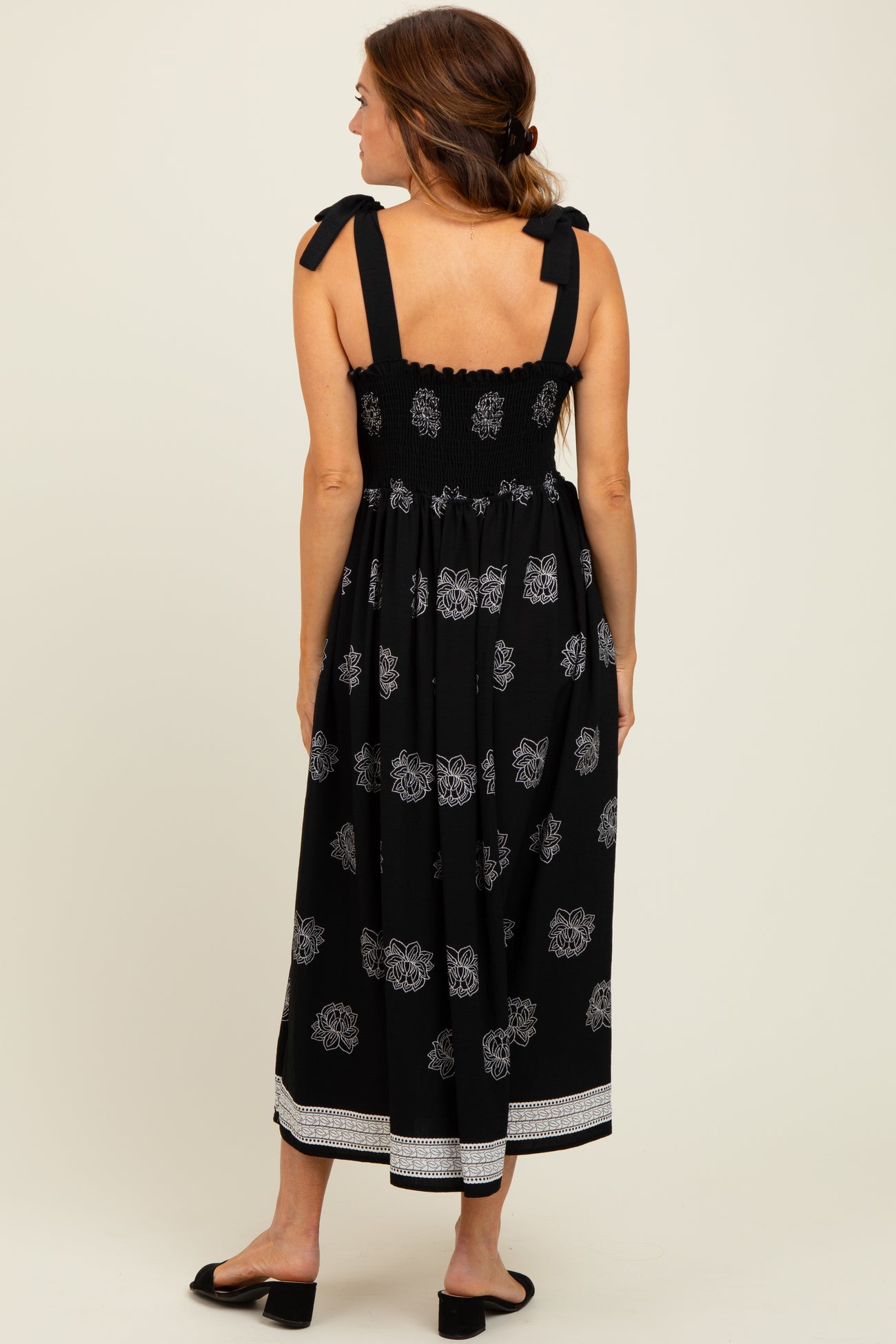 woman wearing a black maxi dress with floral pattern and tie shoulder straps, shown from the back