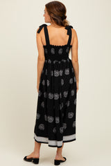 woman wearing a black maxi dress with floral pattern and tie shoulder straps, shown from the back