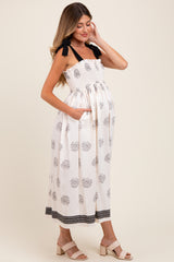 woman wearing a white strapless maternity dress with floral print and pockets, showcasing her baby bump