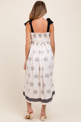 woman wearing a white maternity dress with floral print and black ruffle straps, showing a maternity-friendly design