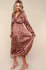 woman wearing a brown leopard print maternity dress with a v-neck and long sleeves, holding the hem while smiling