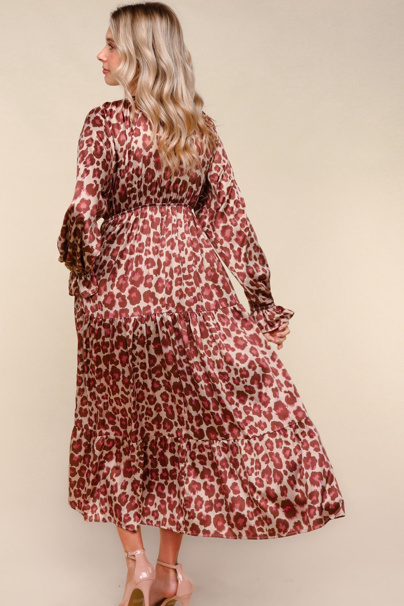 woman wearing a long leopard print maxi dress with flared sleeves and a tiered skirt, facing away from the camera