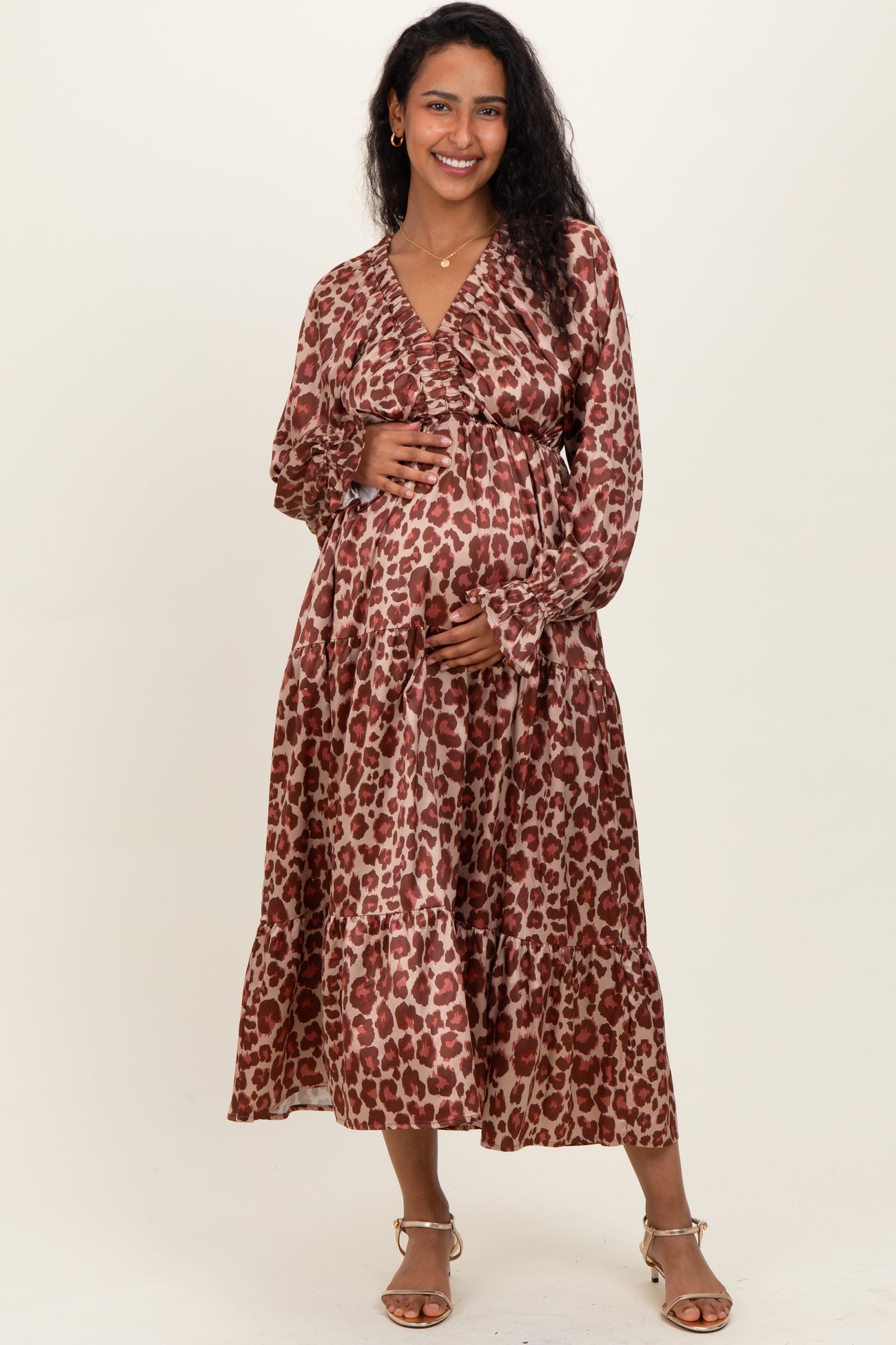 woman wearing a brown leopard print maternity dress, holding her baby bump with long sleeves and a flattering tiered skirt