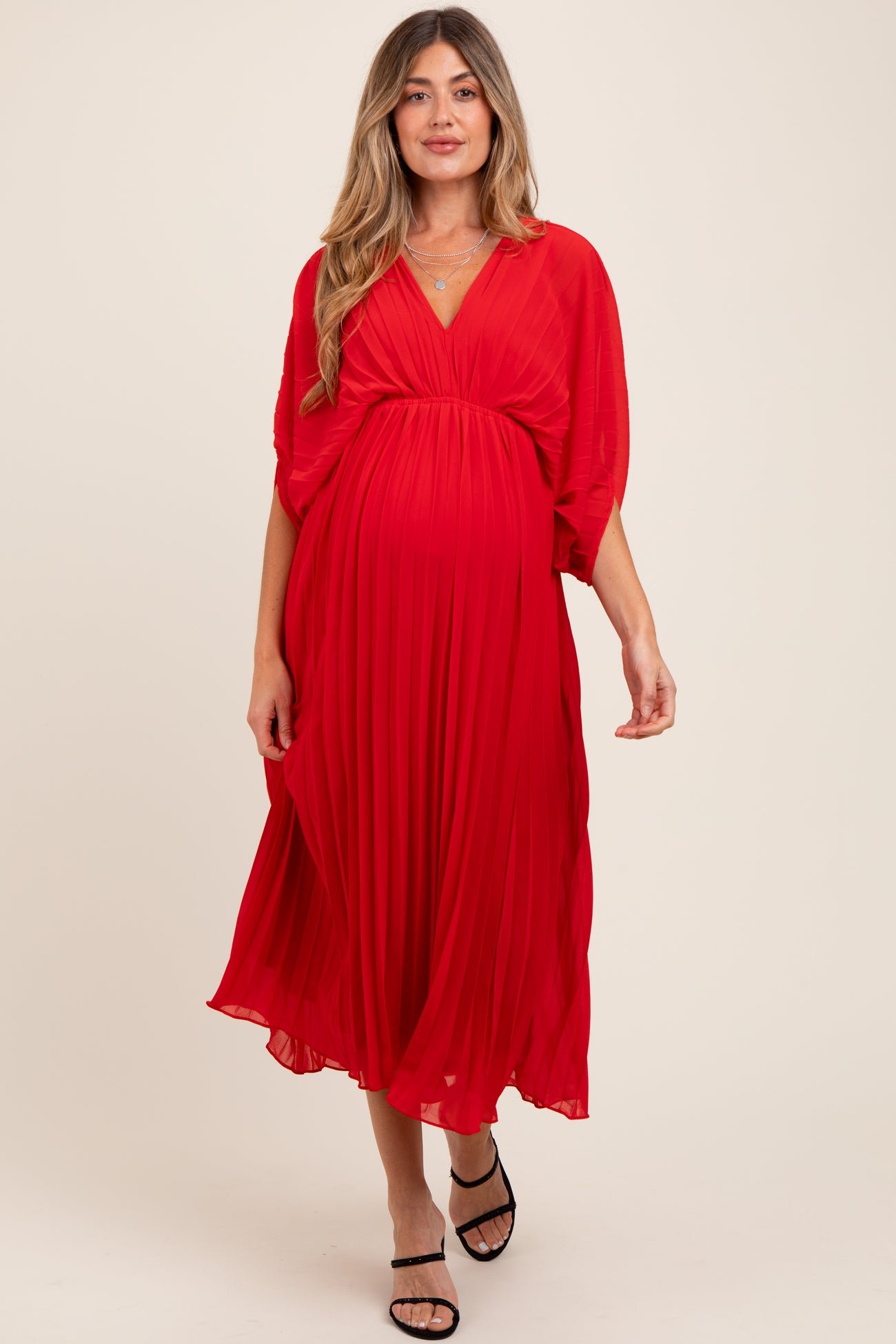 woman wearing a flowing red maternity dress with pleated skirt and v-neckline, showcasing her baby bump