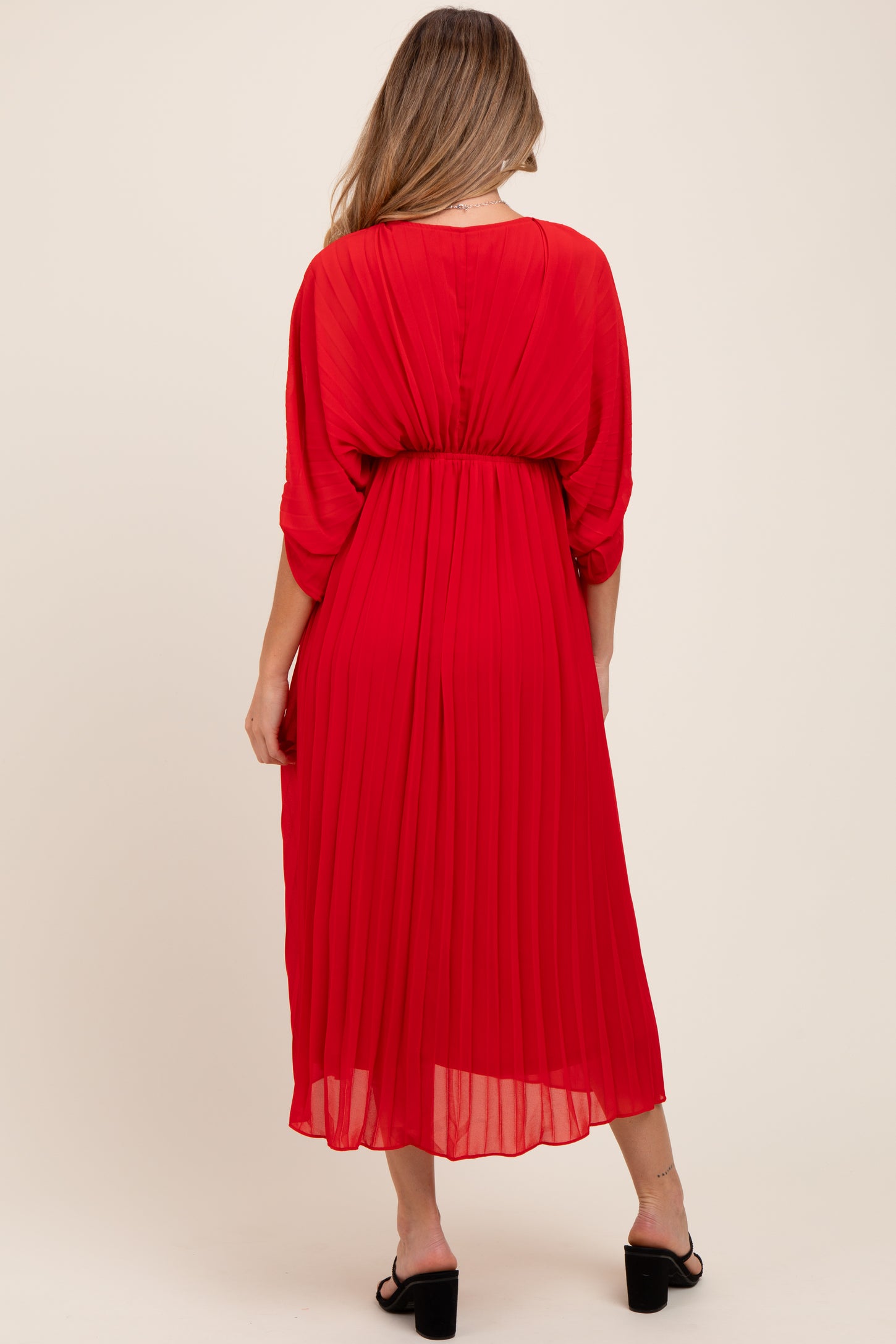 woman wearing a red pleated maternity dress with a relaxed fit and mid-calf length, showing her baby bump from behind