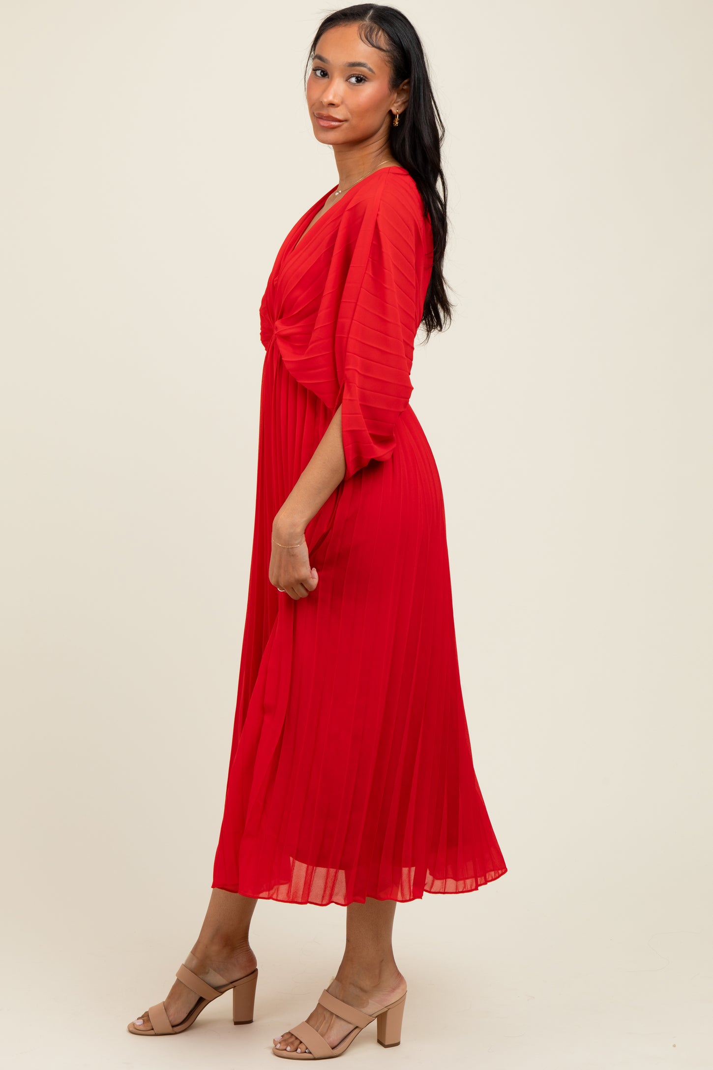 woman wearing a red pleated midi dress with a v-neck and flutter sleeves, standing sideways against a neutral background