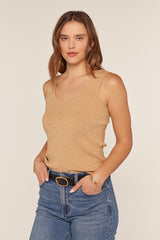 woman wearing a tan sleeveless knit top paired with high-waisted blue jeans, standing with hands on hips