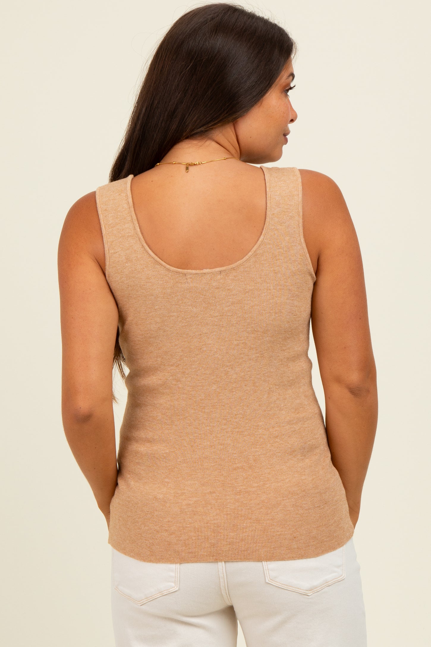 woman wearing a beige maternity tank top, view from the back, styled with white pants