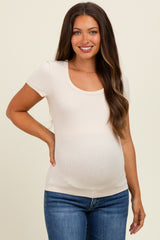 woman wearing a light beige short sleeve maternity top and showing her baby bump