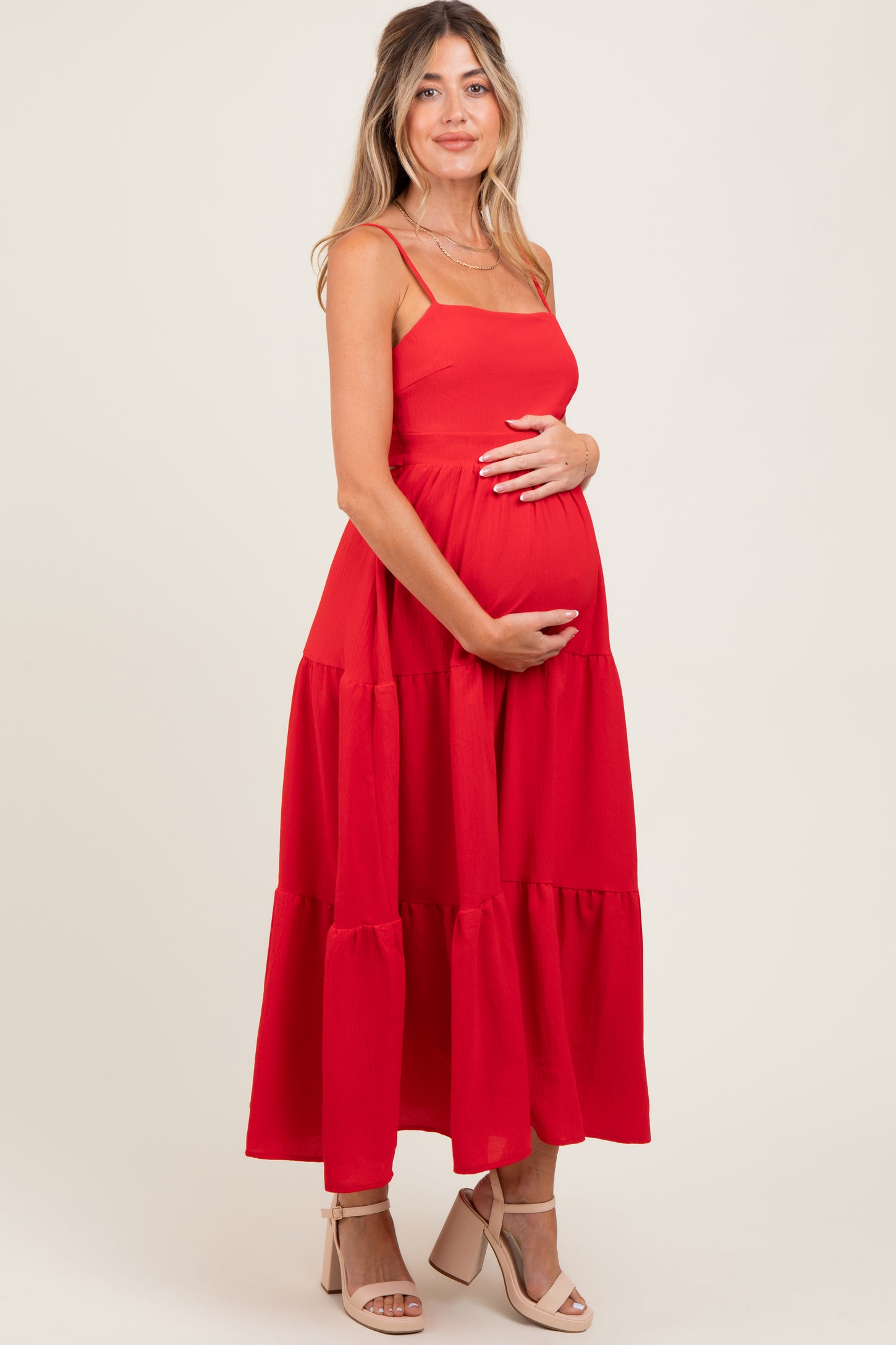 woman wearing a red maternity maxi dress with tiered ruffles, gently cradling her baby bump
