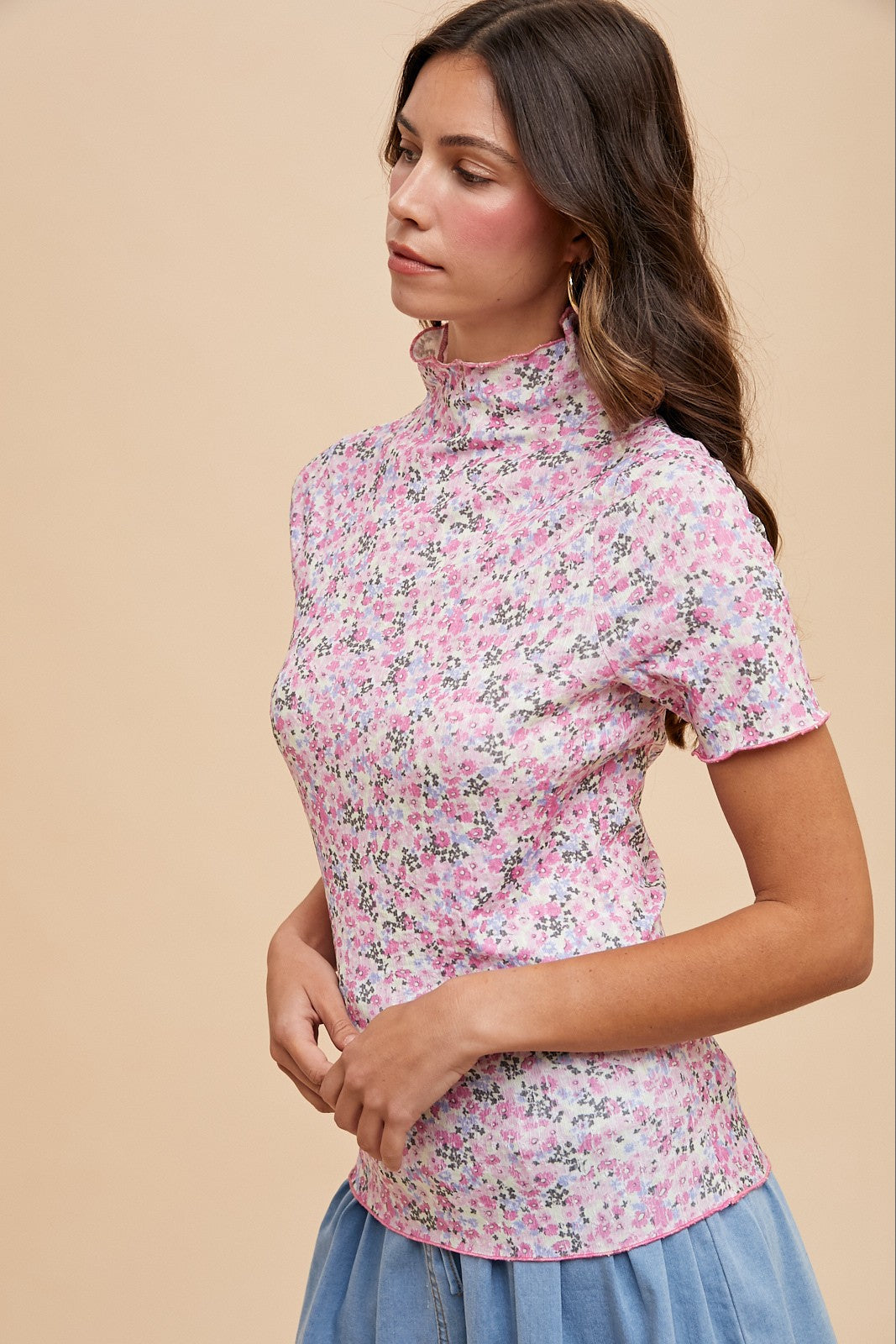 woman wearing a pink floral short sleeve top with a mock neck and side hand on her hip