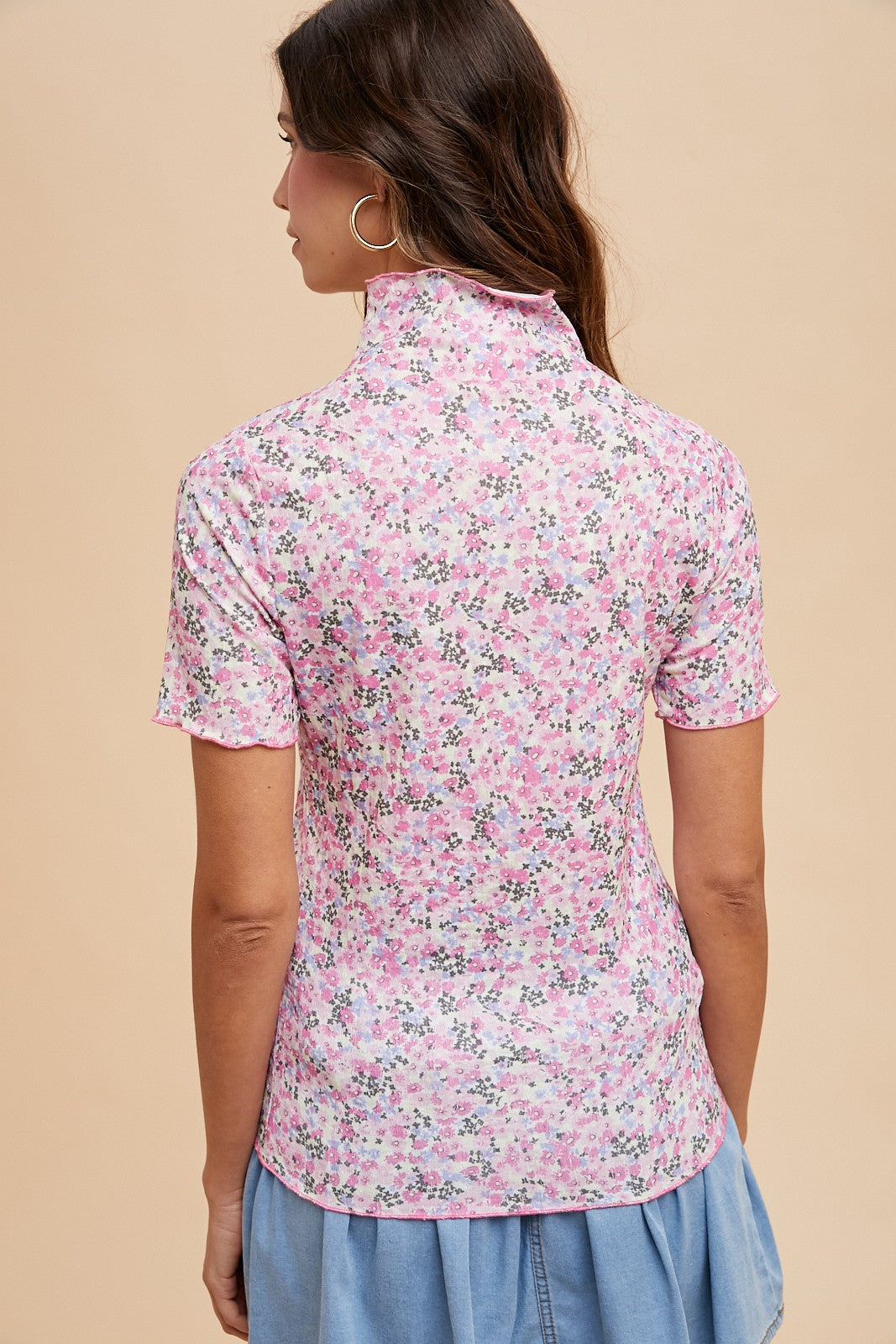 woman wearing a pink floral short sleeve top with a high neckline and a relaxed fit, viewed from the back