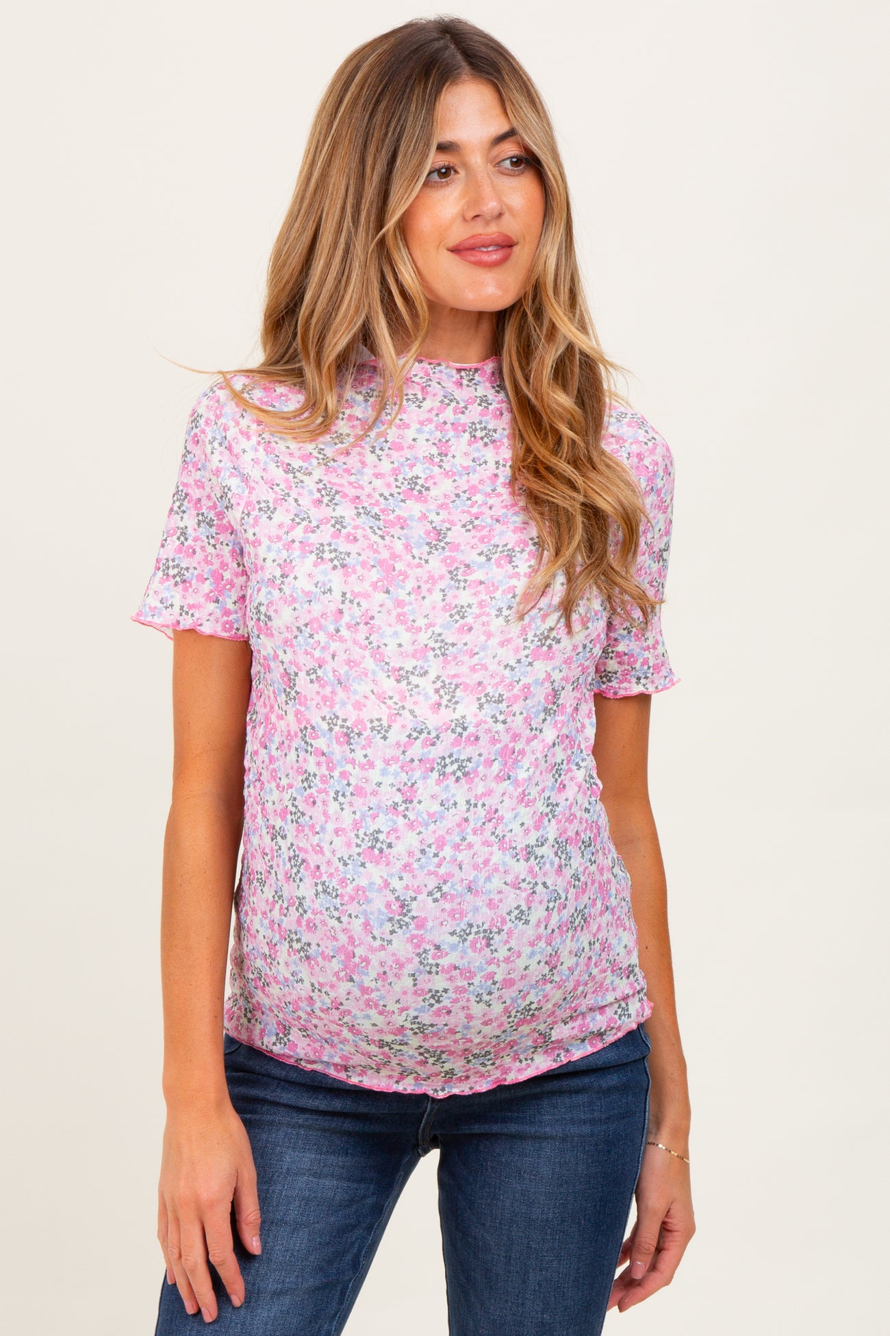 woman wearing a pink floral maternity top with short sleeves and a visible baby bump, paired with dark jeans