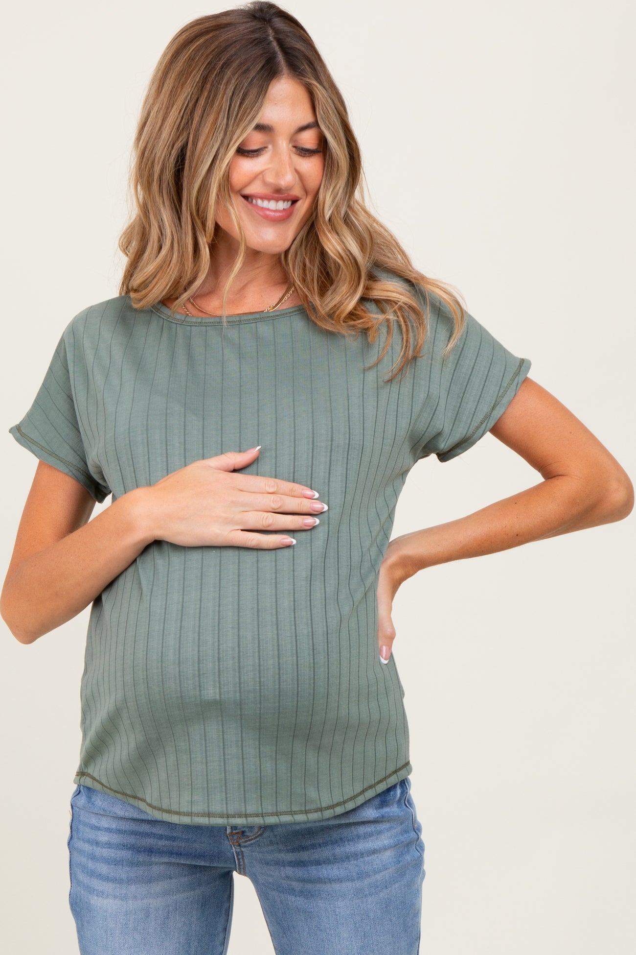 woman wearing a green maternity top with ribbed texture, gently holding her baby bump