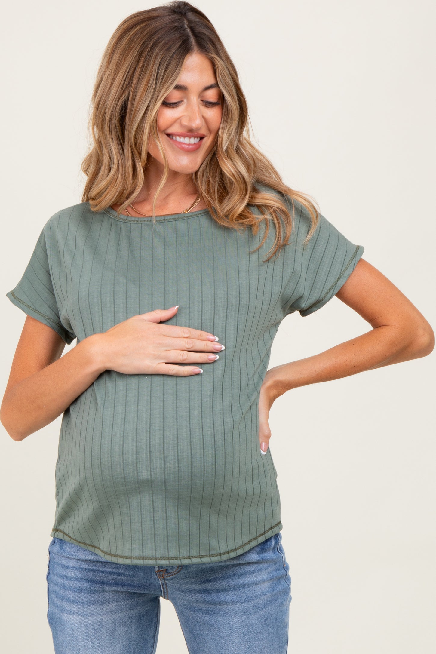 woman wearing a green maternity top with ribbed texture, gently holding her baby bump