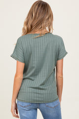 woman wearing a green ribbed maternity top, showing the back view with rolled sleeves and a relaxed fit