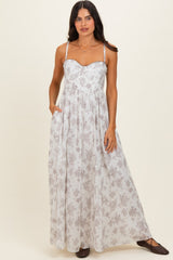 woman wearing a white floral maxi dress with a sweetheart neckline and spaghetti straps, standing with hands in pockets